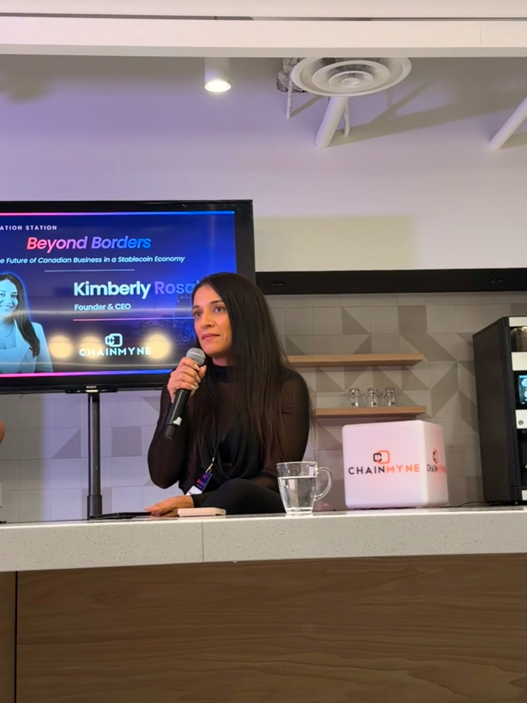 Kimberly Rosales speaking into a microphone at a Beyond Borders session, her name on the screen behind her